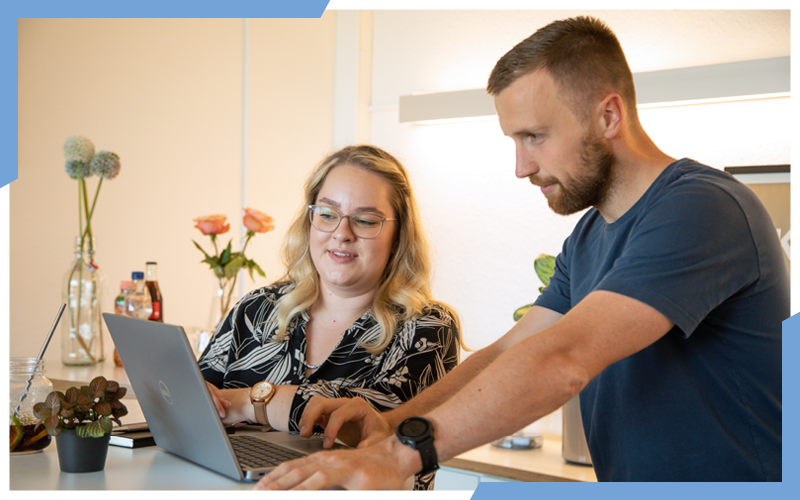 Eine junge Frau und ein Mann stehen an einem Hochtisch, vor ihnen ist ein Laptop, in den die beiden schauen. Im Hintergund sieht man ein regal und Blumen. | © die media GmbH